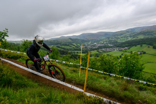 Rider on track at British National Downhill Series, view of Llangollen, Wales countryside in backdrop.