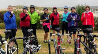 Group of female cyclists, standing behind a row of bikes, all appear to be eating ice cream cones