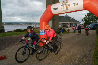 Two cyclists crossing the finishing line of a cycle event. Fiona is the cyclist wearing the orange helmet