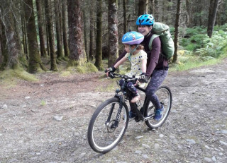 Jenny on a bike with her daughter, cycling on a trail through a forest