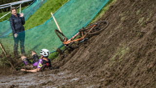 A rider at the bottom of a muddly slope, having fallen off of his bike during a cyclo-cross race