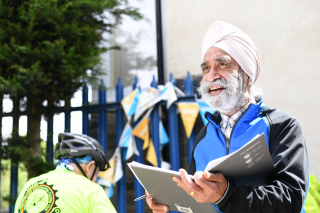 A male cycling coach running a session, holding a notebook