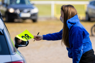 A volunteer issues a rider with their race number in a drive-through sign-on area.