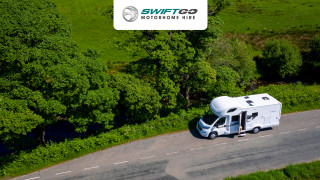 Aerial view of swift motorhome hire on a country road on a sunny day parked next to green trees and fields